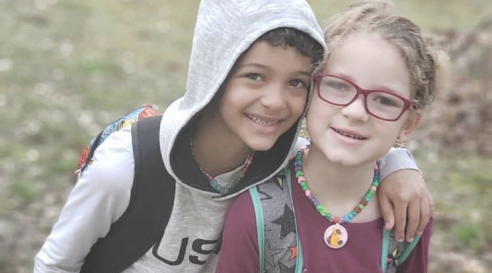 Young boy in gray hooding with his arm around his younger sister smiling.