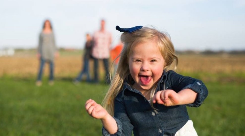 Young girl with down syndrome dancing in a field with her family behind her