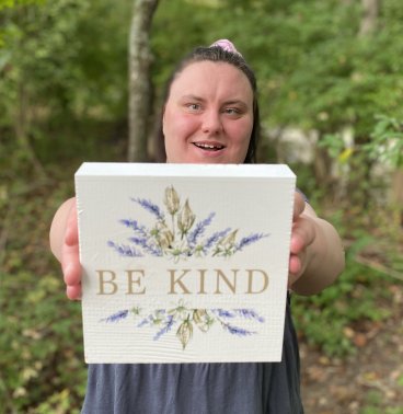 A woman with cerebral palsy holding a sign that says "be kind".