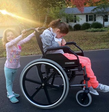 A young girl pushing a wheelchair with a teenager in it.