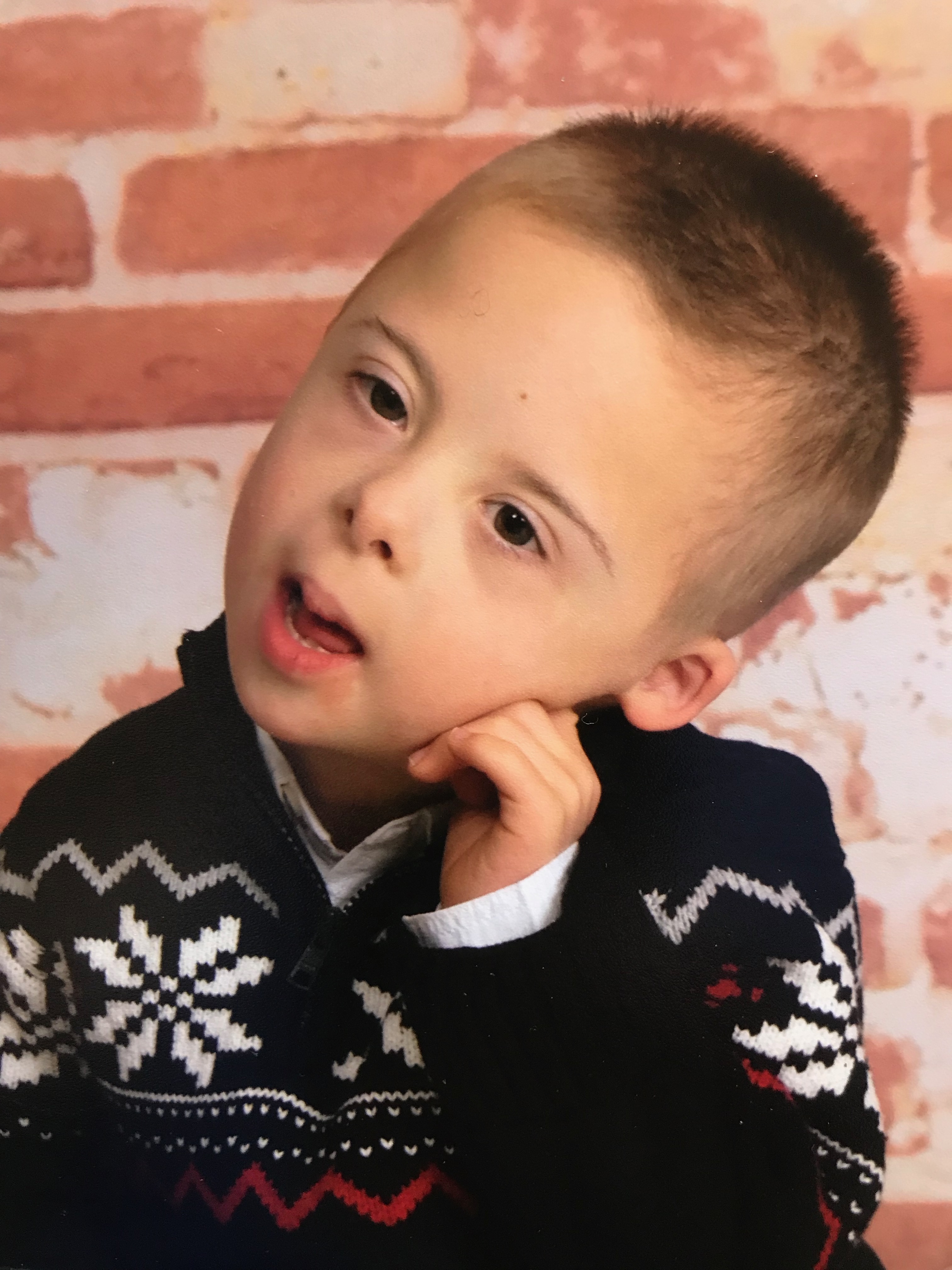 Little boy posing for a picture with his head resting on his hand while wearing a black Christmas sweater.